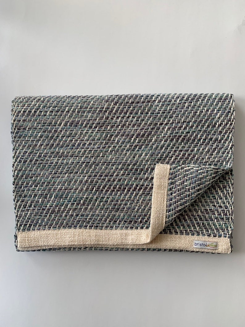 May include: A folded blue and white woven rug with a cream colored border and a "Bristol" label.