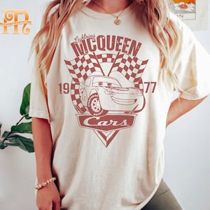 May include: A white t-shirt with a red graphic of Lightning McQueen from the Disney Pixar movie Cars. The graphic includes the text "Lightning McQueen", "Cars", and "19-77".
