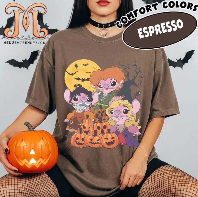 May include: Espresso-colored t-shirt featuring a Halloween-themed graphic with cartoon characters, pumpkins, a full moon, and bats. The shirt has the words "COMFORT COLORS" and "ESPRESSO" printed on it. A carved pumpkin is held in the foreground.