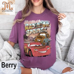 May include: Purple t-shirt with a vintage-style graphic of Lightning McQueen and Mater from the movie Cars. The graphic includes the text "Radiator Springs".