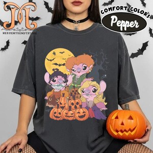 May include: Dark gray Comfort Colors t-shirt featuring a Halloween-themed graphic. The design includes cartoon characters, jack-o'-lanterns, a full moon, and bats. The shirt also has the text "Pepper" and "Comfort Colors".