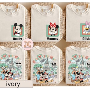 May include: Ivory t-shirts with Disney character designs. One shirt features Mickey Mouse with "Daddy", another has Minnie Mouse with "Mommy", and a third has Daisy Duck with "Olivia". The bottom shirts have a Disney World graphic.