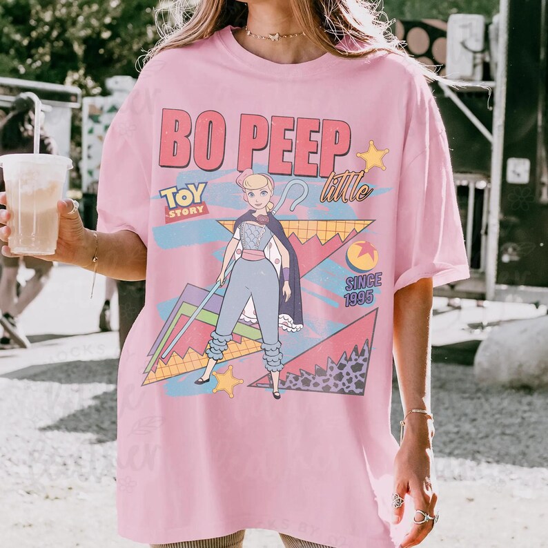 May include: Pink t-shirt featuring a graphic of Bo Peep from Toy Story. The design includes the text "Bo Peep Little Toy Story Since 1995" with a cartoon illustration of the character. The shirt has short sleeves and a relaxed fit.