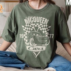 May include: A green t-shirt with a graphic of Lightning McQueen from the movie Cars. The graphic includes the text "Lightning McQueen", "1977", and "Cars".