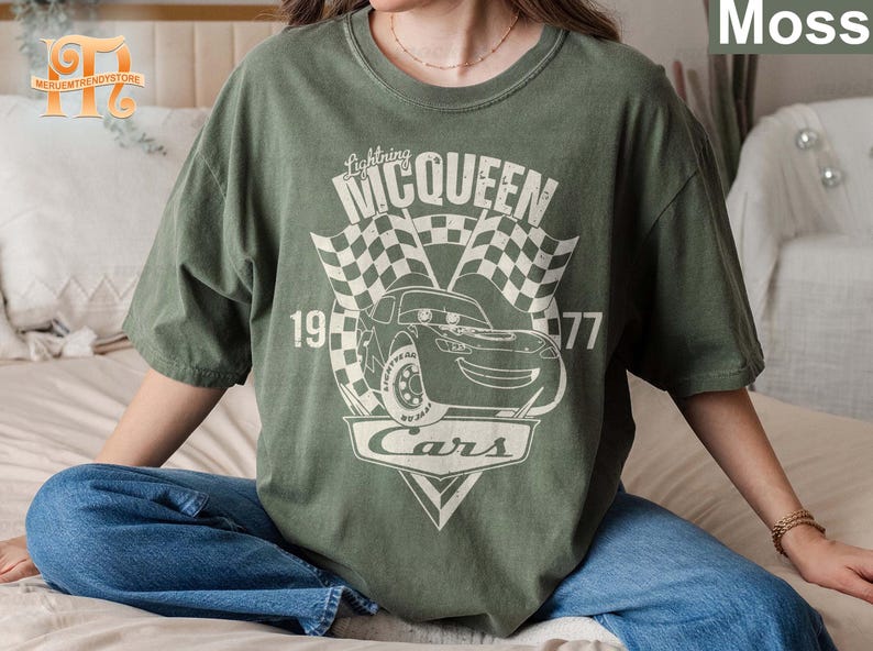 May include: A green t-shirt with a graphic of Lightning McQueen from the movie Cars. The graphic includes the text "Lightning McQueen", "1977", and "Cars".
