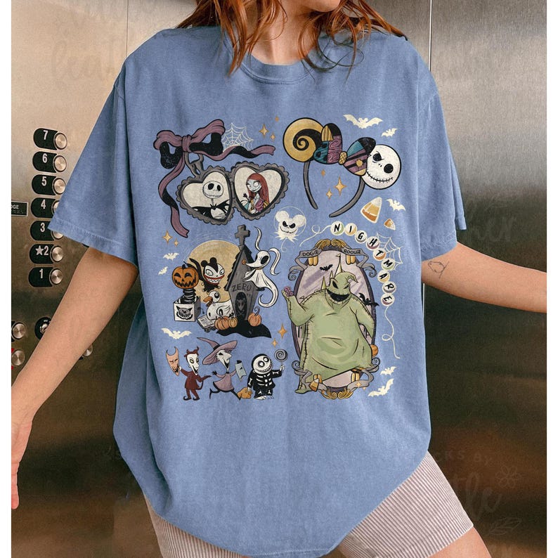 May include: A light blue short-sleeve t-shirt featuring a multi-colored graphic print of characters and icons from The Nightmare Before Christmas, including Jack Skellington, Sally, Oogie Boogie, and Zero, with the text Nightmare.
