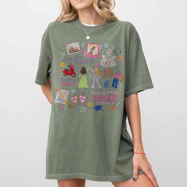 May include: An olive green t-shirt featuring a vibrant graphic. The design incorporates illustrations of a scooter, figures, and the text "THIS IS WHAT DREAMS ARE MADE OF". The t-shirt has short sleeves and a loose fit.