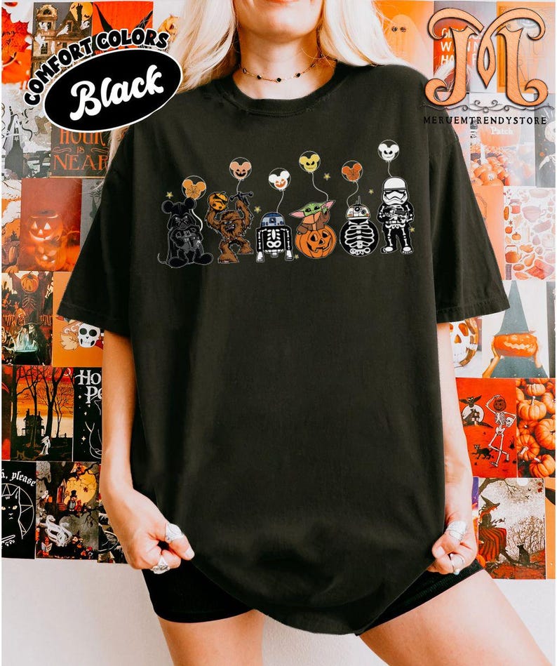 Op de afbeelding: Zwart T-shirt met een afbeelding van Star Wars-personages als Halloween-decoraties. De personages zijn onder meer Mickey Mouse, Chewbacca, R2-D2, Baby Yoda, een pompoen, een skelet en een Stormtrooper, elk met een ballon. De woorden "COMFORT COLORS" en "Black" zijn gedrukt.