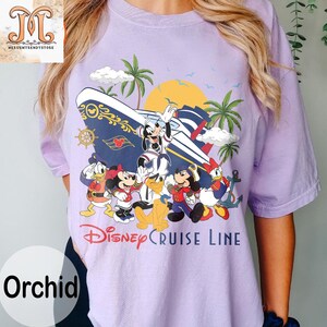 May include: Orchid-colored t-shirt featuring a Disney Cruise Line design. The graphic includes Mickey Mouse, Minnie Mouse, Donald Duck, and other characters with a cruise ship, palm trees, and a sunset. The text "Disney Cruise Line" is printed below the characters.