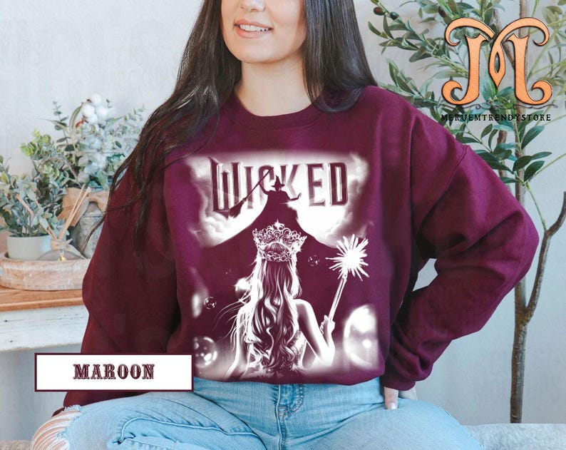 May include: Maroon sweatshirt featuring a graphic from the musical "Wicked." The design includes the word "Wicked" in white, a silhouette of a witch on a broom, and a princess with a crown and wand. The word "Maroon" is printed at the bottom.