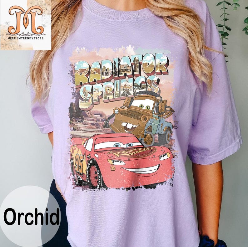 May include: A purple t-shirt with a graphic of Lightning McQueen and Mater from the movie Cars. The graphic includes the text "Radiator Springs".