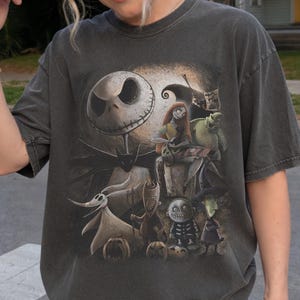 May include: Dark gray t-shirt featuring a graphic of characters from The Nightmare Before Christmas. The design includes Jack Skellington, Sally, Zero, and other characters in a detailed illustration. The shirt has a vintage, worn look.