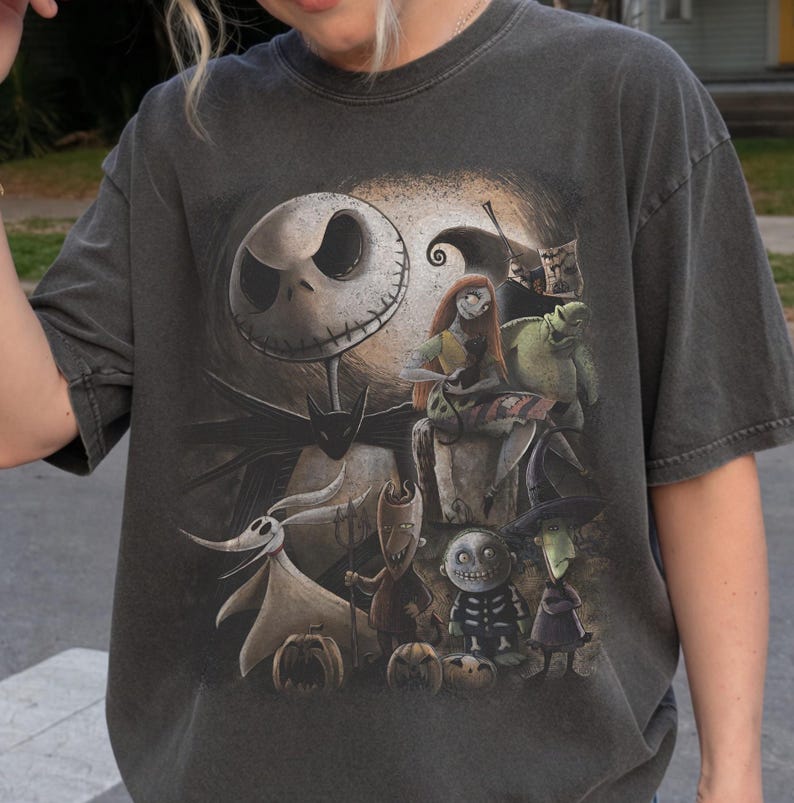 May include: Dark gray t-shirt featuring a graphic of characters from The Nightmare Before Christmas. The design includes Jack Skellington, Sally, Zero, and other characters in a detailed illustration. The shirt has a vintage, worn look.