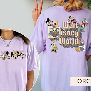 Puede incluir: Una camiseta morada con un gr&aacute;fico de Mickey Mouse y sus amigos frente a un arco&iacute;ris con el texto "Walt Disney World".