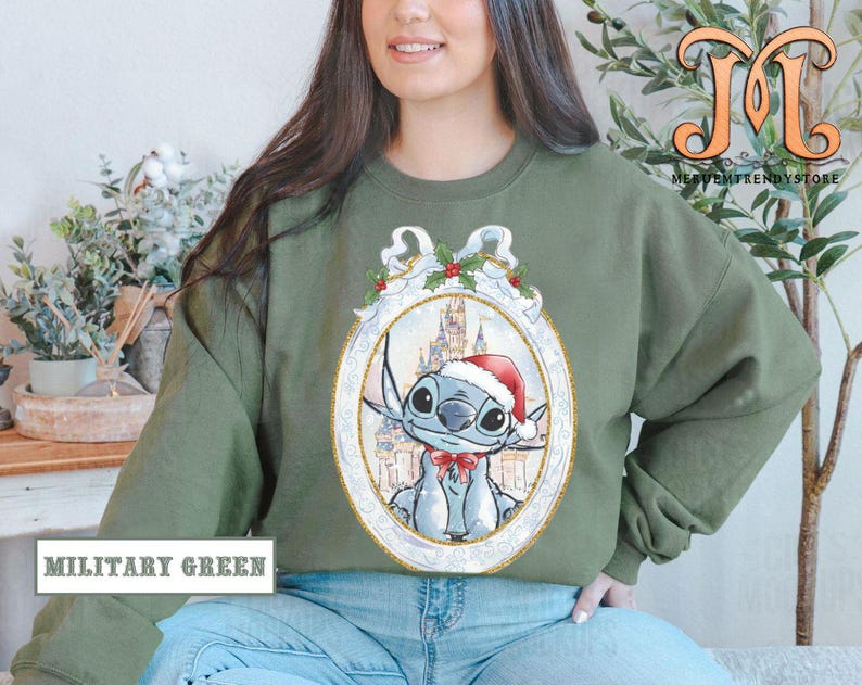 May include: Military green sweatshirt featuring a cartoon character in a Santa hat and bow tie, set against a castle backdrop within a decorative frame. The sweatshirt has the text "MILITARY GREEN" at the bottom.