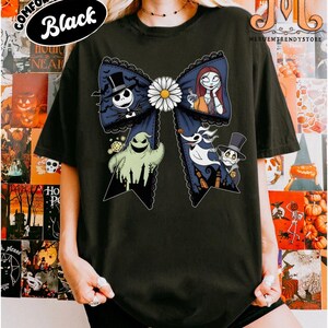 Peut inclure: T-shirt noir avec un grand motif de n&oelig;ud orn&eacute; de personnages d'un film d'animation populaire. Le n&oelig;ud comporte une marguerite blanche au centre et est d&eacute;cor&eacute; avec Jack Skellington, Sally et d'autres personnages. Le texte "COMFORT COLORS Black" est imprim&eacute; en haut &agrave; gauche.
