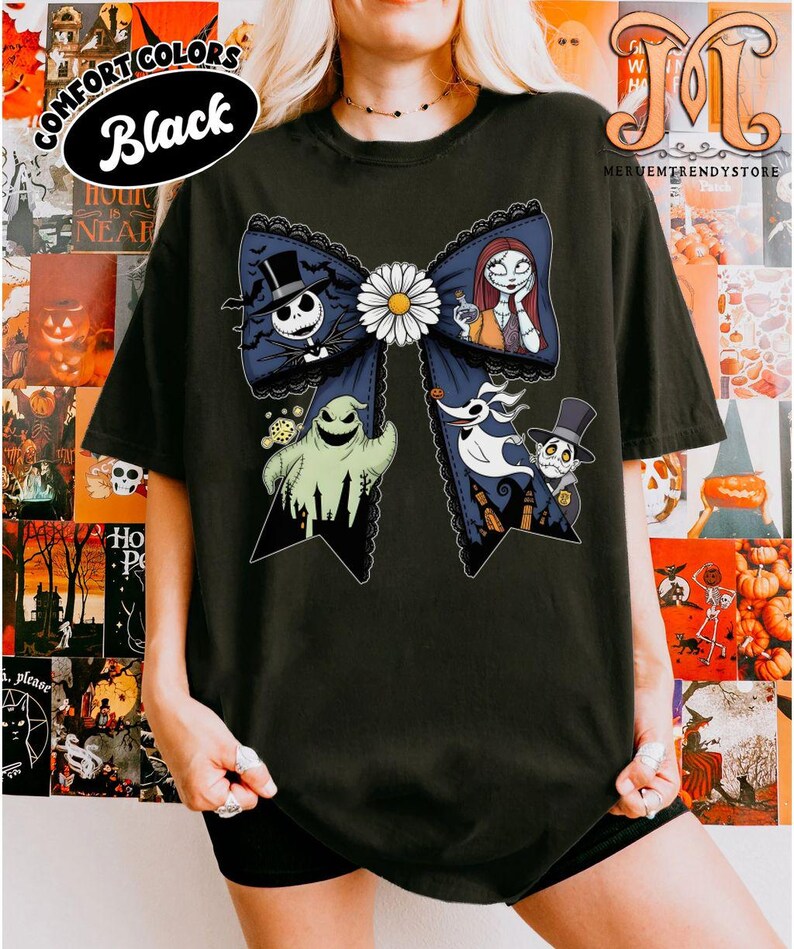 Peut inclure: T-shirt noir avec un grand motif de n&oelig;ud orn&eacute; de personnages d'un film d'animation populaire. Le n&oelig;ud comporte une marguerite blanche au centre et est d&eacute;cor&eacute; avec Jack Skellington, Sally et d'autres personnages. Le texte "COMFORT COLORS Black" est imprim&eacute; en haut &agrave; gauche.