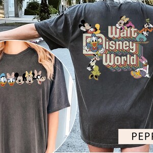 Puede incluir: Dos camisetas grises con tem&aacute;tica de Disney World. Una camiseta presenta una l&iacute;nea de personajes de Disney, incluidos Mickey Mouse, Donald Duck y Goofy. La otra camiseta presenta un gr&aacute;fico de estilo retro con el texto "Walt Disney World" y varios personajes de Disney.