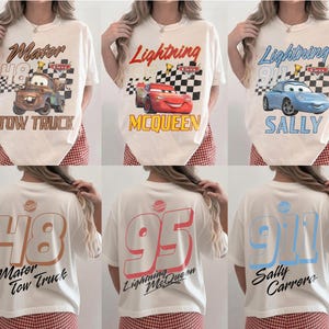 May include: Cream-colored t-shirts featuring Cars movie characters: Mater, Lightning McQueen, and Sally. Each shirt has a graphic on the front and back with character names and numbers. The front graphics include checkered flags.