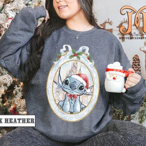 May include: Dark heather gray sweatshirt featuring a festive Stitch design in a decorative frame. Stitch is wearing a Santa hat and bow tie. The sweatshirt also has the text "DARK HEATHER". A Santa mug is held in the hand.