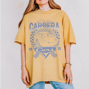 May include: Mustard yellow t-shirt featuring a graphic of Sally Carrera from the movie Cars. The design includes the text "Sally Carrera" above the car image, with "Cars" and the numbers "19" and "51" below.