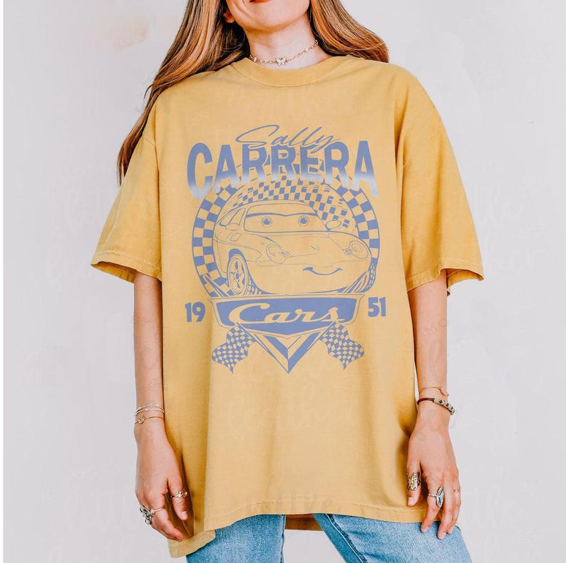 May include: Mustard yellow t-shirt featuring a graphic of Sally Carrera from the movie Cars. The design includes the text "Sally Carrera" above the car image, with "Cars" and the numbers "19" and "51" below.