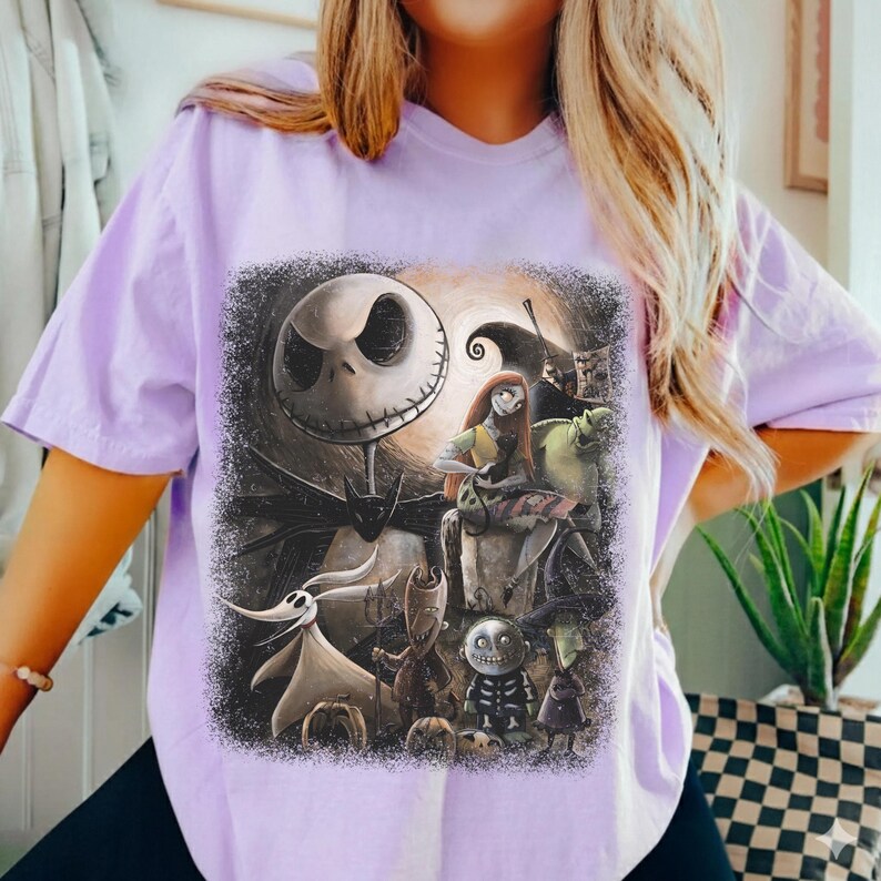 May include: A light purple t-shirt featuring a graphic from the movie "The Nightmare Before Christmas." The design includes Jack Skellington, Sally, and other characters in a dark, spooky scene. The shirt has short sleeves and a relaxed fit.