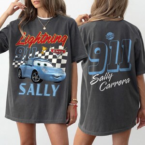 May include: Dark gray t-shirt featuring a blue cartoon car with the text "Lightning 911 Cars" and "SALLY" on the front. The back of the shirt displays "911 Sally Carrera" in blue and white.