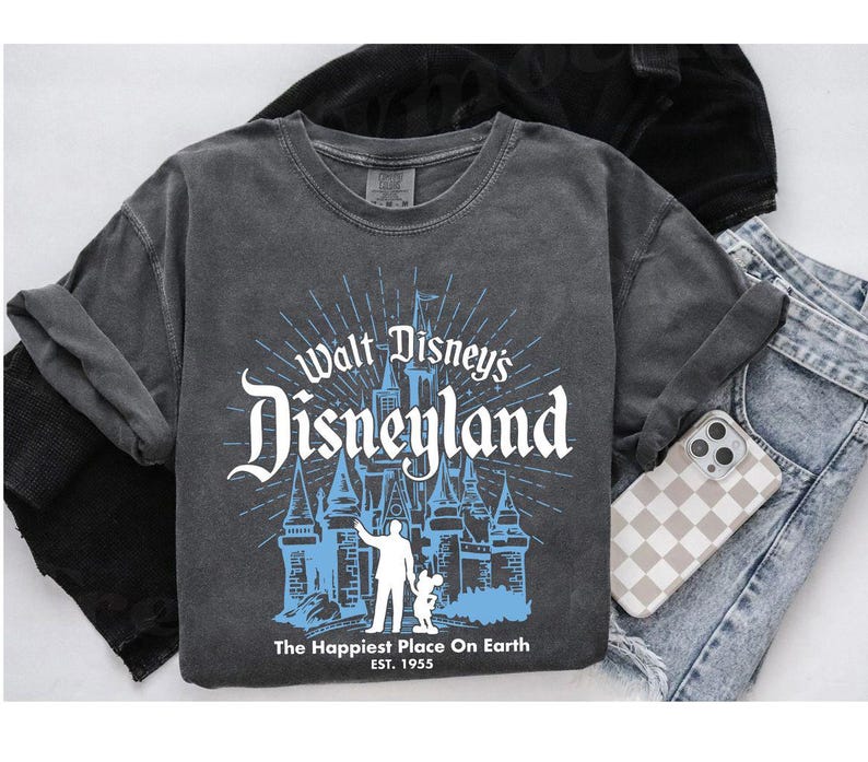 Puede incluir: Una camiseta gris de manga larga con un gr&aacute;fico desgastado del castillo de Disneyland y el texto "Walt Disney's Disneyland". El gr&aacute;fico es en blanco y azul claro. La camiseta tambi&eacute;n tiene el texto "The Happiest Place On Earth EST. 1955".