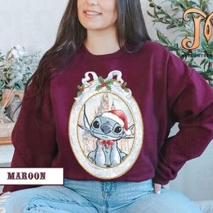 May include: Maroon sweatshirt featuring a cartoon character wearing a Santa hat and bow tie, set within an ornate oval frame. The frame includes a castle backdrop and holly accents. The text "MAROON" is displayed at the bottom.