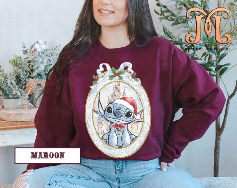 May include: Maroon sweatshirt featuring a cartoon character wearing a Santa hat and bow tie, set within an ornate oval frame. The frame includes a castle backdrop and holly accents. The text "MAROON" is displayed at the bottom.