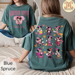 May include: A teal blue t-shirt with a pink and white graphic of Mickey Mouse as a sorcerer on the front. The back of the shirt features a pattern of Mickey Mouse dressed as a witch in various poses.
