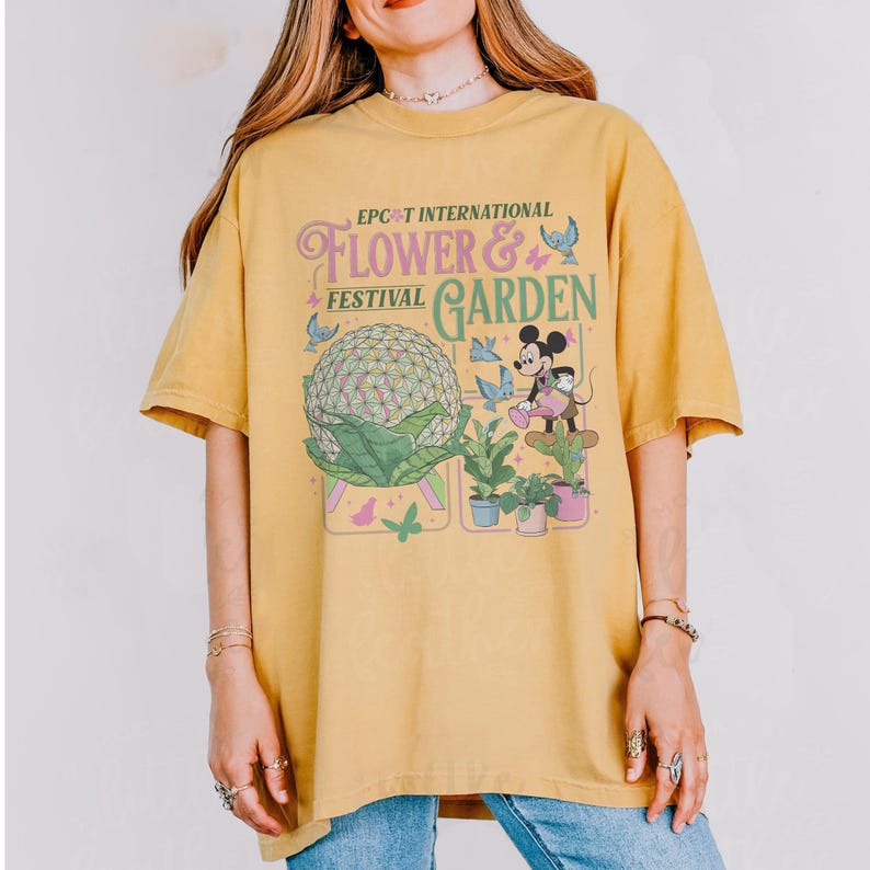 May include: Mustard yellow t-shirt featuring the text "EPCOT INTERNATIONAL FLOWER & GARDEN FESTIVAL" with a graphic of Mickey Mouse, plants, and a large sphere. The shirt has short sleeves and a crew neck.