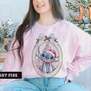 May include: Light pink sweatshirt featuring a cartoon character in a Santa hat and bow tie, set within an ornate frame with holly accents. The sweatshirt has long sleeves and the text "LIGHT PINK" is displayed at the bottom.