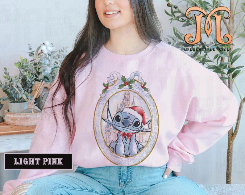 May include: Light pink sweatshirt featuring a cartoon character in a Santa hat and bow tie, set within an ornate frame with holly accents. The sweatshirt has long sleeves and the text "LIGHT PINK" is displayed at the bottom.