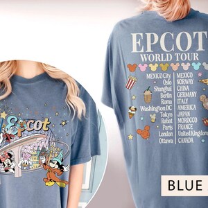 May include: Blue jean t-shirt featuring a graphic of Mickey Mouse and friends on a ride at Epcot. The back of the shirt displays the text "Epcot World Tour" and a list of countries and cities.