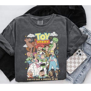 Puede incluir: Sudadera gris oscuro con un gr&aacute;fico colorido de personajes de la pel&iacute;cula animada "Toy Story". El dise&ntilde;o incluye a Woody, Buzz Lightyear y otros personajes. Tambi&eacute;n se ve el texto "TOY STORY" y "YOU'VE GOT A FRIEND IN ME".