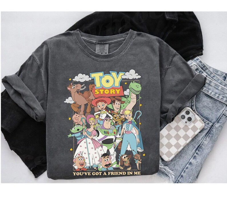 Puede incluir: Sudadera gris oscuro con un gr&aacute;fico colorido de personajes de la pel&iacute;cula animada "Toy Story". El dise&ntilde;o incluye a Woody, Buzz Lightyear y otros personajes. Tambi&eacute;n se ve el texto "TOY STORY" y "YOU'VE GOT A FRIEND IN ME".