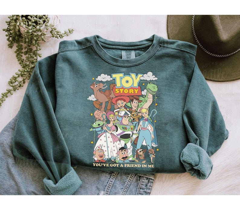 Puede incluir: Sudadera de color verde azulado con un estampado colorido de personajes de la pel&iacute;cula "Toy Story". El dise&ntilde;o incluye las palabras "Toy Story" y "You've Got a Friend in Me". La sudadera tiene mangas largas y cuello redondo.