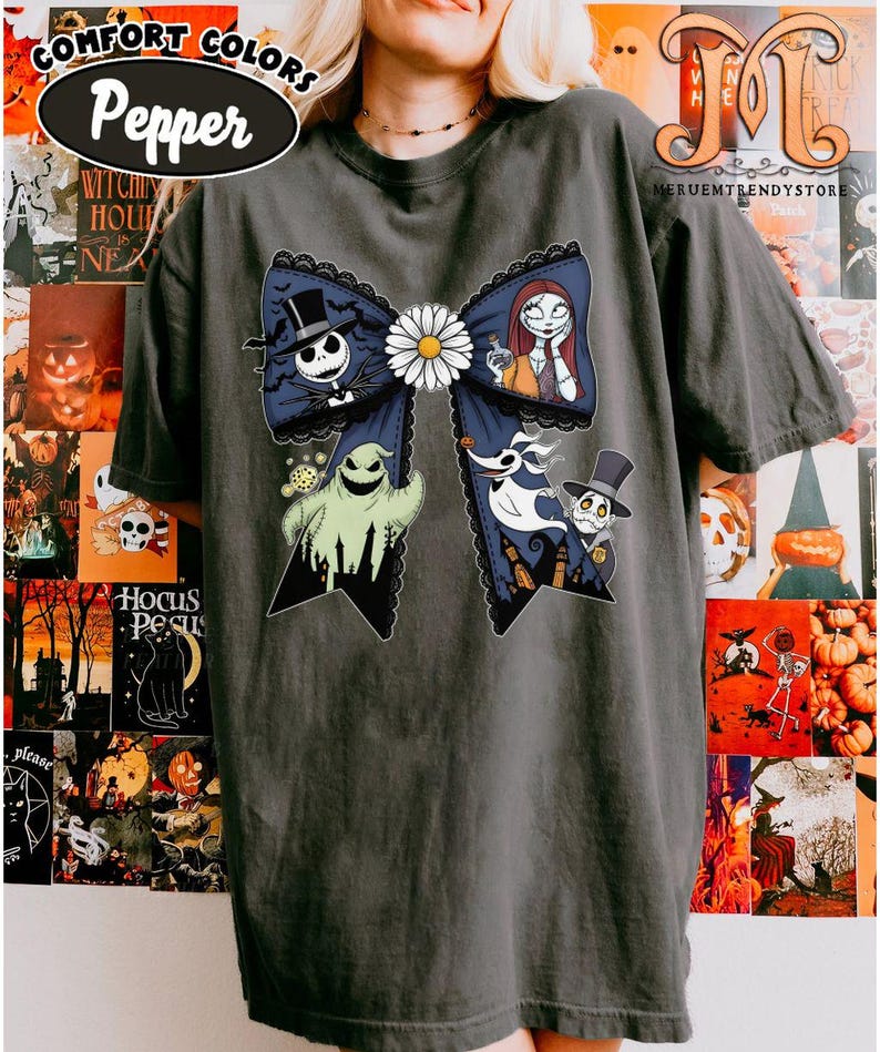 Peut inclure: T-shirt gris fonc&eacute; avec un grand motif de n&oelig;ud orn&eacute; de personnages de L'&Eacute;trange No&euml;l de Monsieur Jack. Le n&oelig;ud bleu marine est bord&eacute; de dentelle noire et orn&eacute; d'une marguerite blanche. Les personnages incluent Jack Skellington, Sally, Zero et Oogie Boogie.