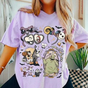 May include: A light purple t-shirt featuring a graphic print of characters from The Nightmare Before Christmas, including Jack Skellington, Sally, Oogie Boogie, and Zero, surrounded by bats, pumpkins, and a decorative mirror frame.