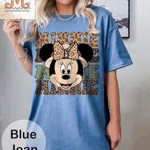 May include: A blue jean t-shirt with a cartoon image of Minnie Mouse wearing a safari hat. The text "Minnie Me Minnie" is printed on the shirt in a brown, green, and black leopard print.