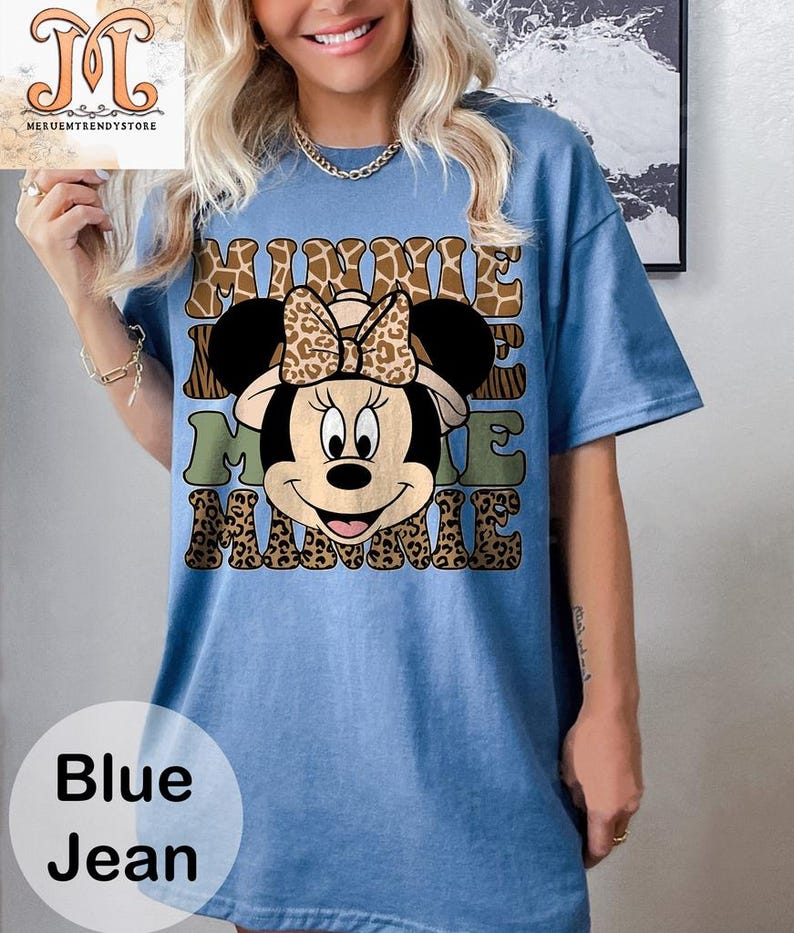 May include: A blue jean t-shirt with a cartoon image of Minnie Mouse wearing a safari hat. The text "Minnie Me Minnie" is printed on the shirt in a brown, green, and black leopard print.