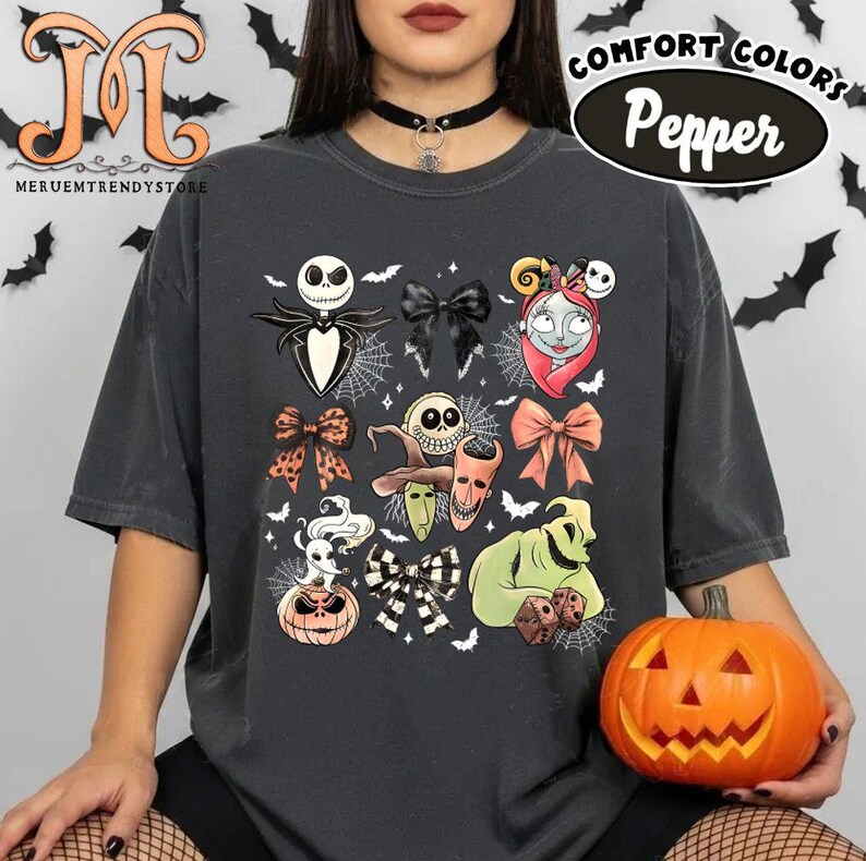 Puede incluir: Camiseta gris oscuro con un gr&aacute;fico colorido de personajes de The Nightmare Before Christmas. El dise&ntilde;o incluye a Jack Skellington, Sally y otros elementos ic&oacute;nicos. La camiseta tambi&eacute;n tiene el texto "COMFORT COLORS Pepper".