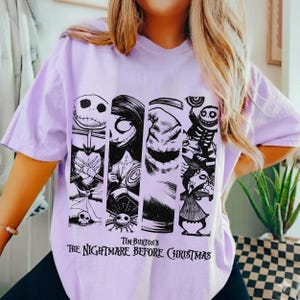 May include: A light purple t-shirt featuring a black graphic print of characters from Tim Burton's The Nightmare Before Christmas. The design consists of four vertical panels displaying Jack Skellington, Sally, Oogie Boogie, and other figures.