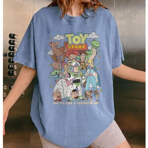 Puede incluir: Camiseta azul claro con un dise&ntilde;o gr&aacute;fico colorido de personajes de la pel&iacute;cula "Toy Story". El dise&ntilde;o incluye el texto "TOY STORY" y "YOU'VE GOT A FRIEND IN ME".