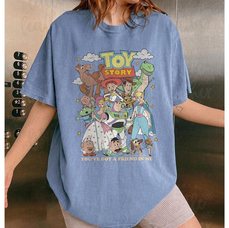 Puede incluir: Camiseta azul claro con un dise&ntilde;o gr&aacute;fico colorido de personajes de la pel&iacute;cula "Toy Story". El dise&ntilde;o incluye el texto "TOY STORY" y "YOU'VE GOT A FRIEND IN ME".