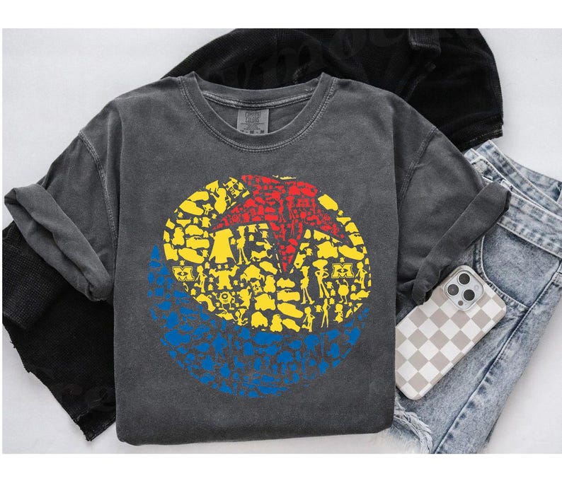 May include: A charcoal gray long-sleeve shirt featuring a circular graphic with a red star and yellow and blue shapes. The shirt is paired with denim jeans and a phone case with a checkered pattern.