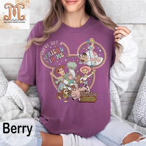 Puede incluir: Camiseta morada con un dise&ntilde;o de cabeza de Mickey Mouse con personajes de la franquicia Toy Story. El texto "You've got a friend in me" est&aacute; dentro de la cabeza de Mickey Mouse. El texto "Woody's Roundup" est&aacute; en la parte inferior del dise&ntilde;o.