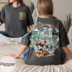 May include: Pepper-coloured t-shirt with a Disney World graphic on the back and a Pluto design on the front. The back graphic includes Mickey Mouse, Minnie Mouse, Donald Duck, and Goofy. The shirt has the text "Custom" on the front.